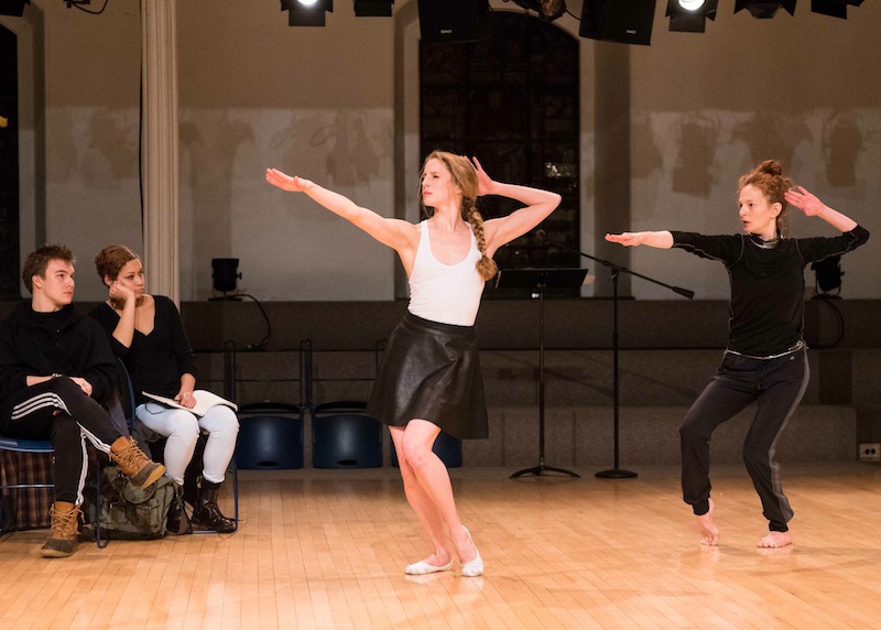 Sterling Hyltin and Jodi Melnick dance with one hand in a salute position and the other outstretched reaching towards the audience